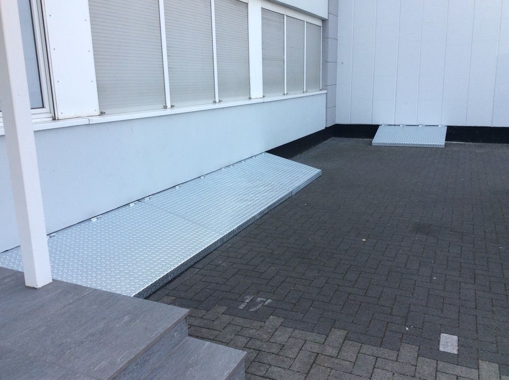 Rampe aus Riffelblech über den Stufen eines Eingangs.