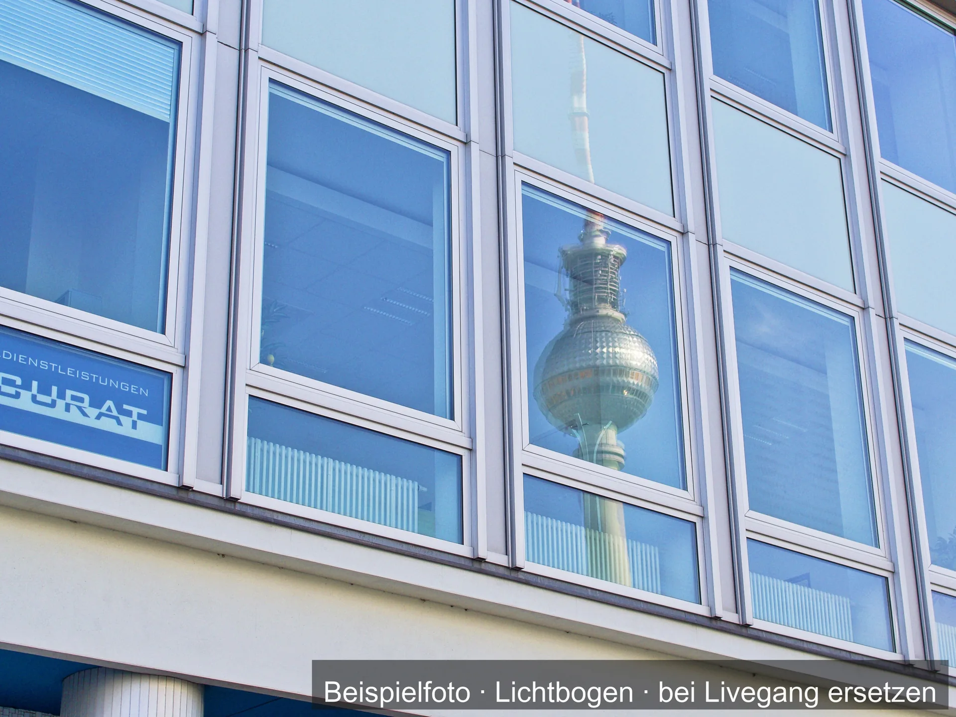 Fensterfront mit schmalen Rahmen, in den Scheiben spiegelt sich ein Sendemast.