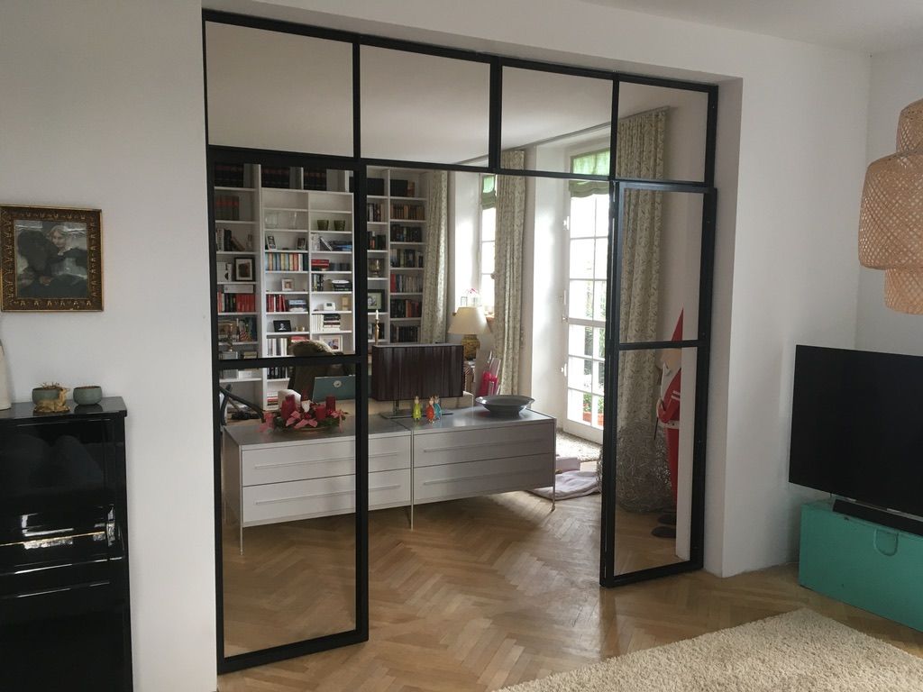 Trennwand aus schwarzen Stahlprofilen und Glas mit Drehtür in einem Wohnraum.
