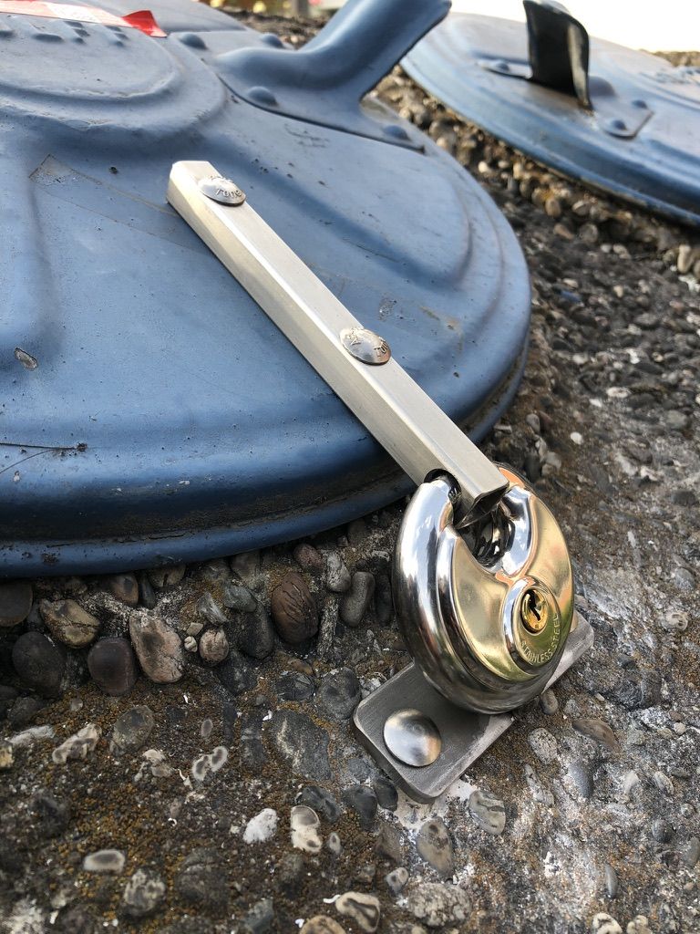 Sicherung aus Flachstahl mit Lasche für ein Vorhängeschloss auf einem Schachtdeckel.